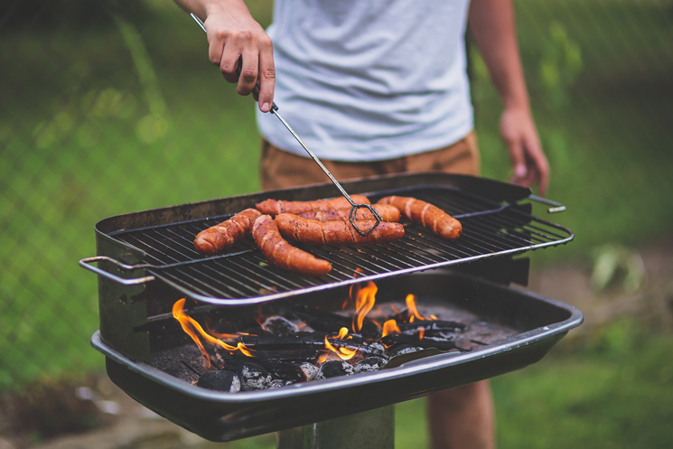 Mann steht am Grill und dreht Bratwürste um